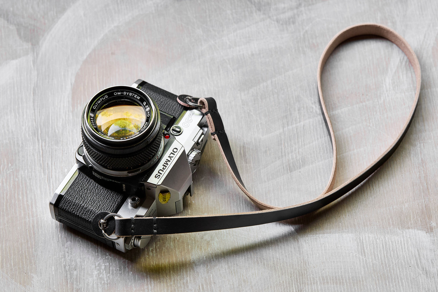 Henry and Wilde Gibson handmade leather camera neck strap in black  attached to a film camera with a protective leather bumper.