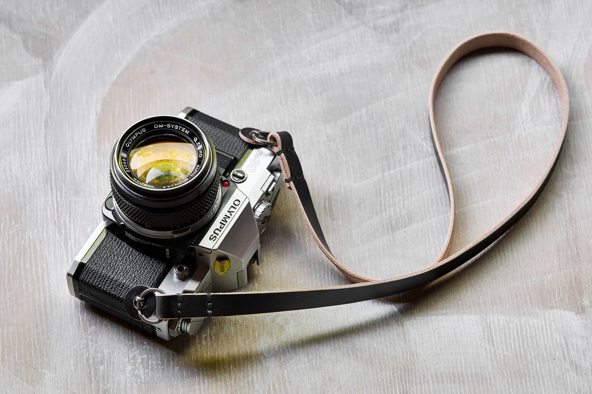 Henry and Wilde Gibson handmade leather camera neck strap in black  attached to a film camera with a protective leather bumper.